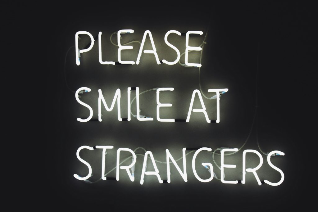 "please smile at strangers" white neon sign on a black background